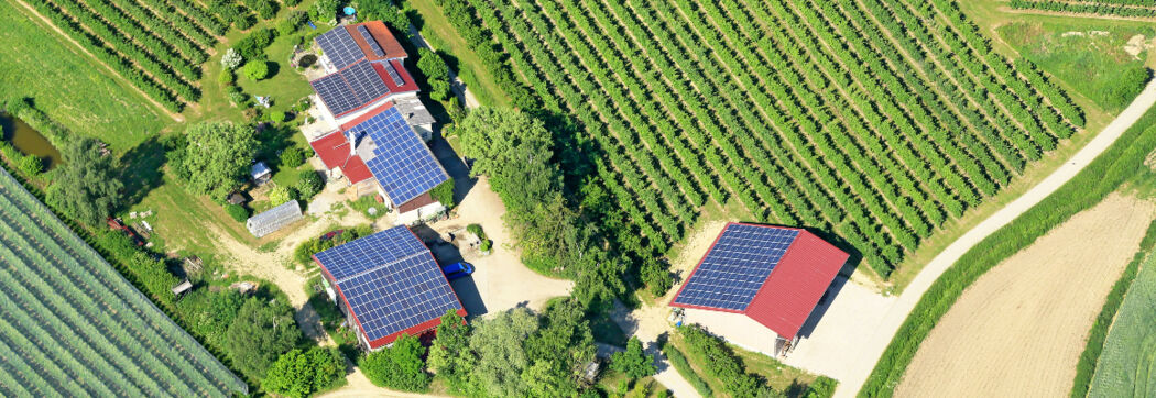 Blick von oben auf einen Hof mit Feldern und Solaranlagen auf den Dächern